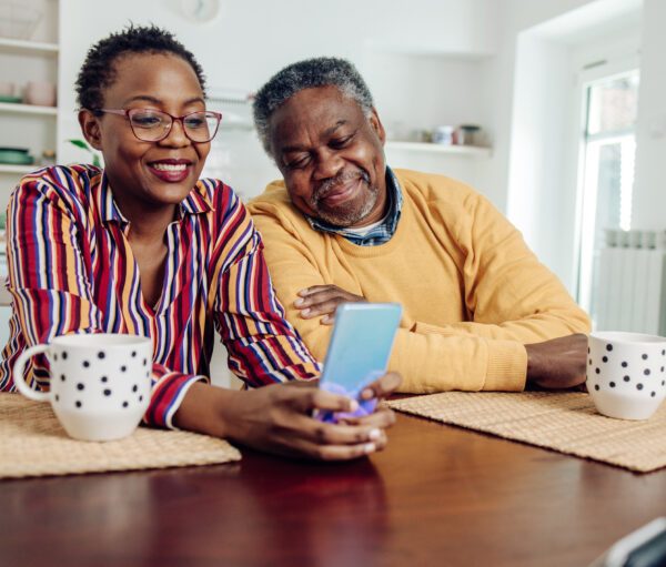 A caregiver and an older man looking at a phone together